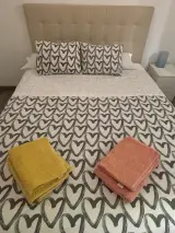 Detalle de la cama doble con toallas amarillas y coral dobladas sobre la colcha de corazones